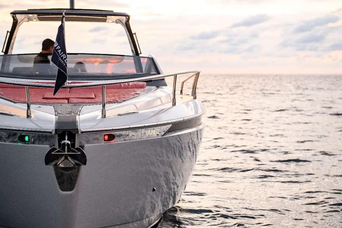 Luxury boat with red seating, green and red navigation lights, and a flag, on calm water during sunset.
